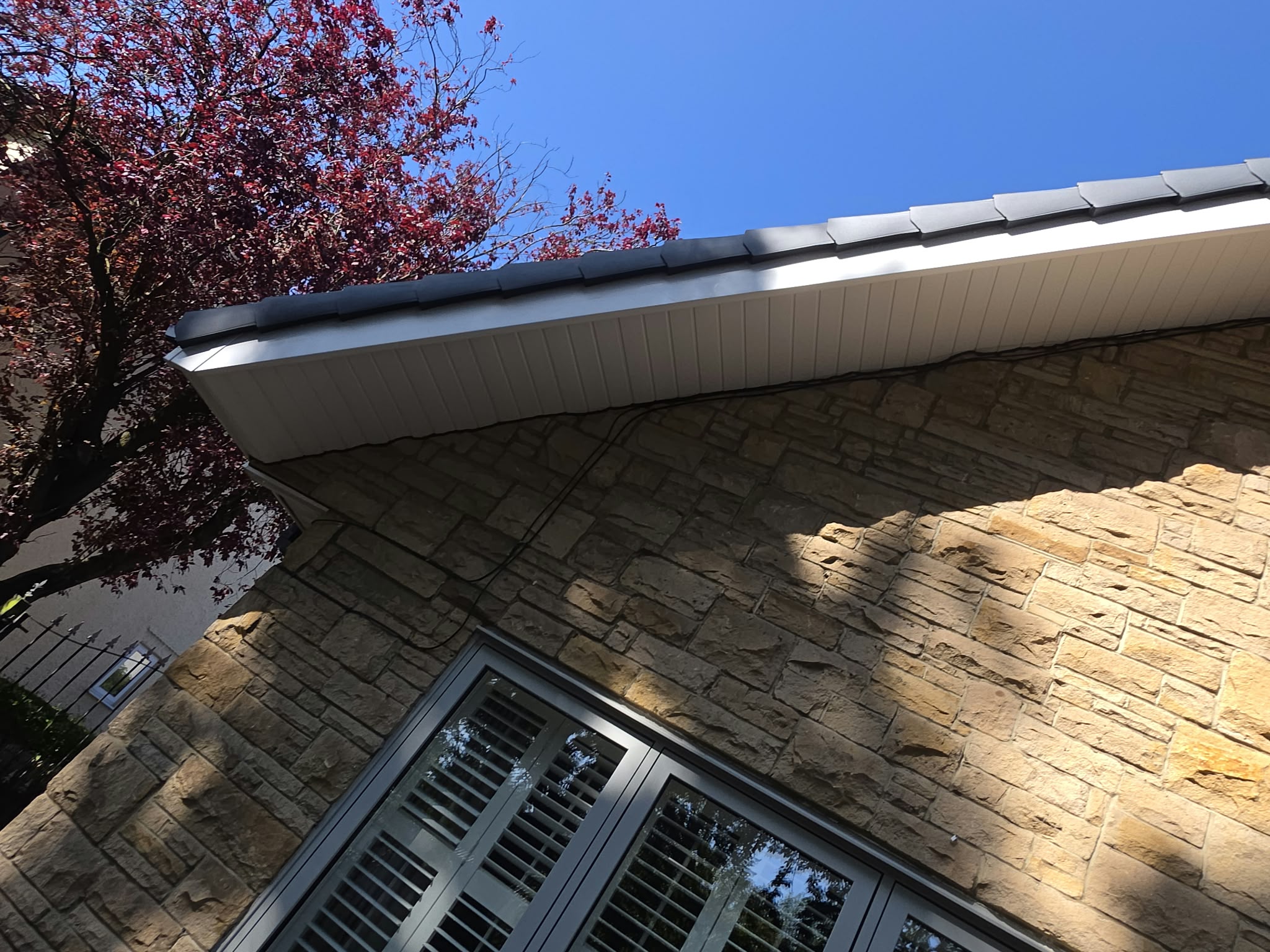White fascia and soffit under the roof tiles of a stone house